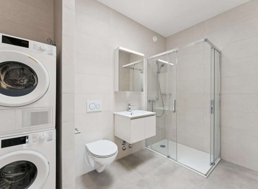 This modern bathroom features a stacked washer and dryer unit, a wall-mounted toilet with a dual-flush system, and a sleek vanity with a sink.