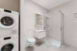 This modern bathroom features a stacked washer and dryer unit, a wall-mounted toilet with a dual-flush system, and a sleek vanity with a sink.