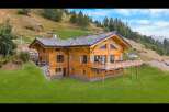 Experience luxury mountain living in this stunning wooden chalet, nestled on a lush green hillside.