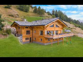 Experience luxury mountain living in this stunning wooden chalet, nestled on a lush green hillside.