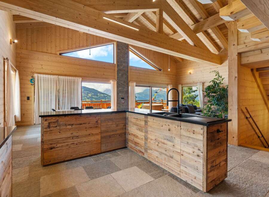 Experience luxurious mountain living in this stunning wooden chalet featuring a modern kitchen with a sleek black countertop and a striking black faucet.
