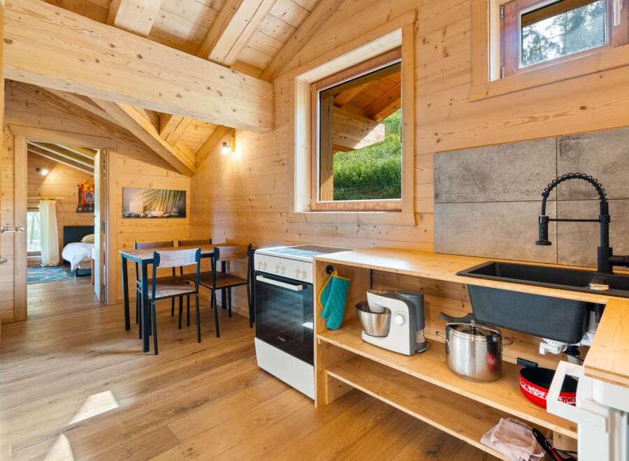 Experience cozy living in this charming wooden cabin, featuring a well-equipped kitchen with modern appliances and a dining area perfect for intimate meals.