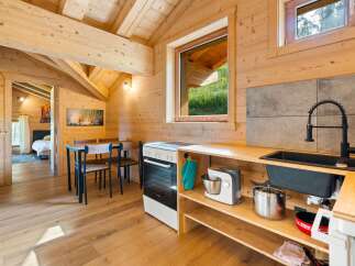 Experience cozy living in this charming wooden cabin, featuring a well-equipped kitchen with modern appliances and a dining area perfect for intimate meals.