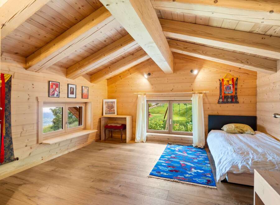 Experience serene living in this charming wooden cabin bedroom, featuring a vaulted ceiling with exposed beams and natural wood finishes throughout.