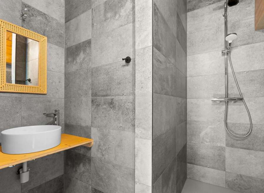 This modern bathroom features a sleek vessel sink atop a rustic wooden vanity, complemented by a woven mirror for a touch of bohemian charm.