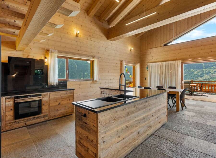 Experience luxurious mountain living in this stunning wooden chalet kitchen, featuring a sleek black granite countertop and a large island with a modern faucet.