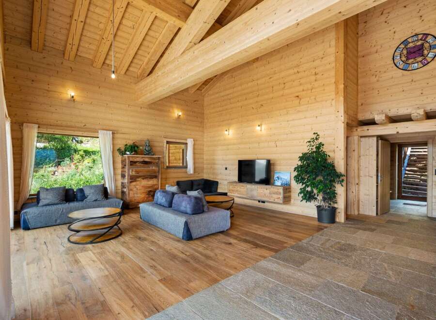 Experience rustic luxury in this stunning wooden chalet living room, featuring exposed beams, a vaulted ceiling, and a cozy fireplace area.