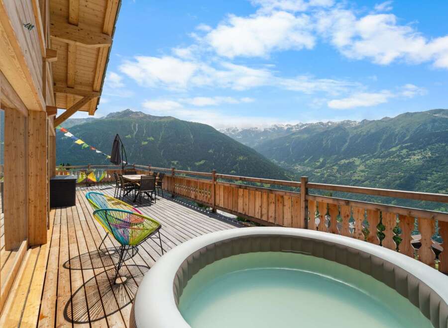 Experience breathtaking mountain views from this stunning chalet deck, complete with a relaxing hot tub and comfortable seating area.