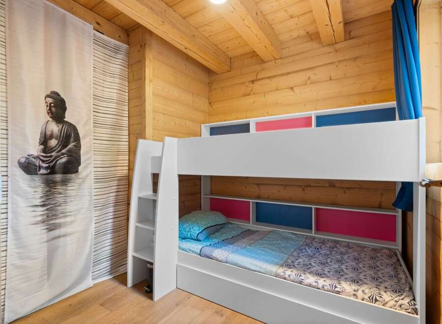 This charming wooden cabin bedroom features a white bunk bed with colorful accents, perfect for a family or guests.