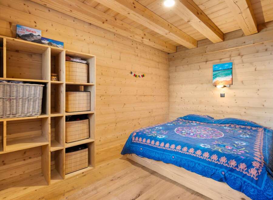 Experience cozy living in this charming wooden cabin bedroom, featuring a comfortable bed adorned with a vibrant blue and pink patterned duvet.