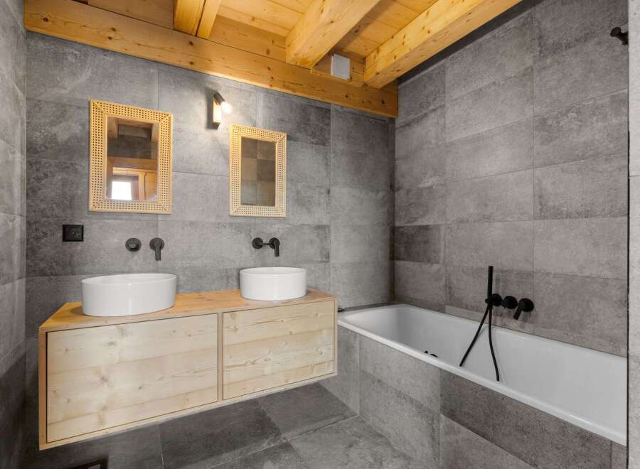 Experience modern mountain living in this stunning bathroom featuring a floating wood vanity with dual vessel sinks and sleek black fixtures.