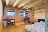 This charming wooden cabin bedroom features a cozy bed with a colorful duvet and ample storage solutions, including a tall shelving unit filled with clothes and a smaller bookshelf with toys.