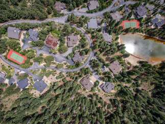 Experience luxury living in this stunning aerial view of a mountain estate featuring multiple modern homes nestled amongst lush pine trees.