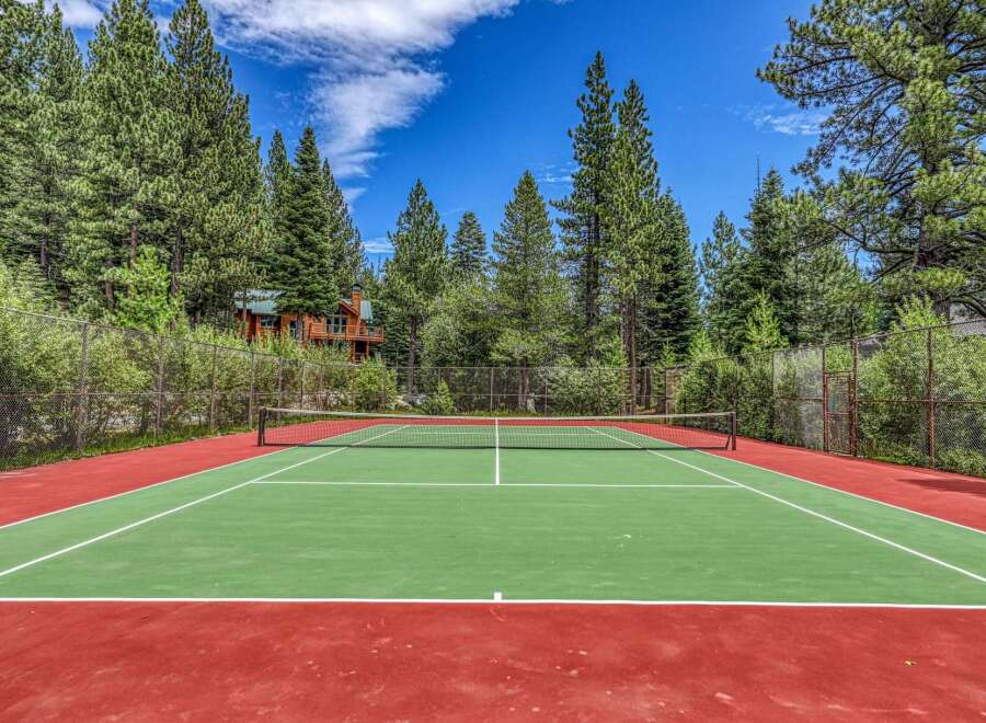 Enjoy outdoor recreation at this stunning property featuring a private tennis court surrounded by lush pine trees.
