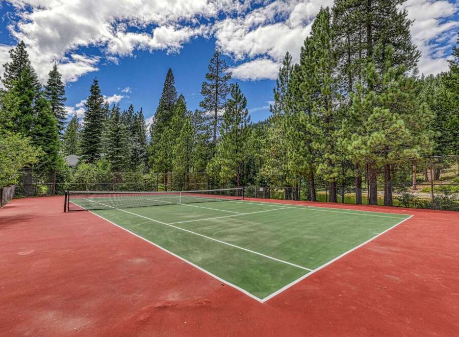 Enjoy outdoor recreation on this beautiful tennis court, surrounded by lush green trees and a clear blue sky.