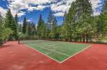 Enjoy outdoor recreation on this beautiful tennis court, surrounded by lush green trees and a clear blue sky.