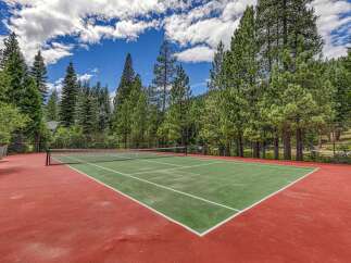 Enjoy outdoor recreation on this beautiful tennis court, surrounded by lush green trees and a clear blue sky.
