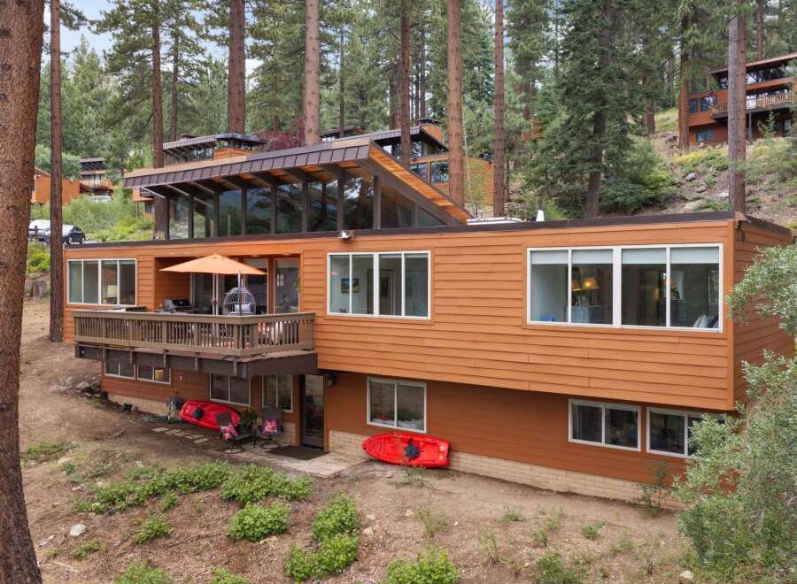 Nestled among tall pine trees, this multi-level home offers a unique architectural design with expansive windows and a warm, wood-paneled exterior.