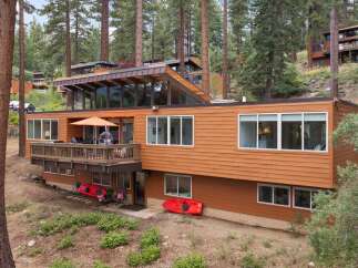 Nestled among tall pine trees, this multi-level home offers a unique architectural design with expansive windows and a warm, wood-paneled exterior.