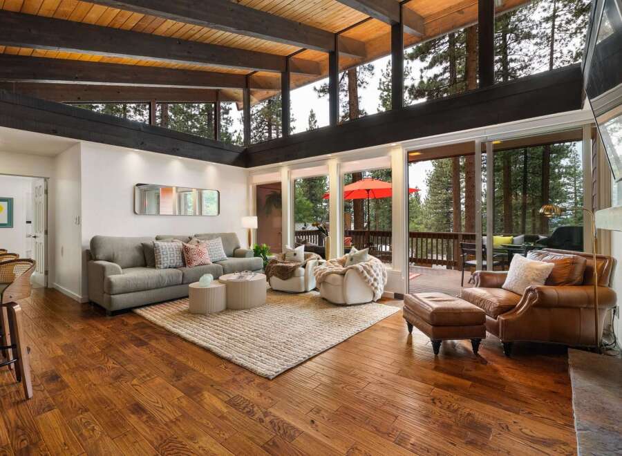 Experience breathtaking forest views from this stunning living room, featuring a vaulted wood-beamed ceiling and expansive windows.