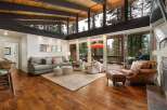 Experience breathtaking forest views from this stunning living room, featuring a vaulted wood-beamed ceiling and expansive windows.