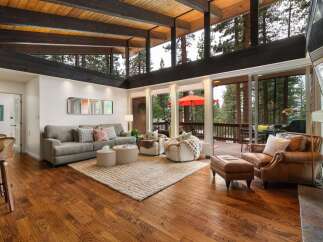 Experience breathtaking forest views from this stunning living room, featuring a vaulted wood-beamed ceiling and expansive windows.