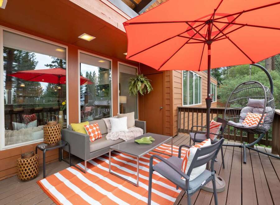 Enjoy outdoor living on this spacious deck featuring a comfortable seating area with a gray sofa, accent chairs, and a coffee table, all complemented by a vibrant orange and white striped rug.