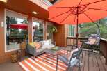 Enjoy outdoor living on this spacious deck featuring a comfortable seating area with a gray sofa, accent chairs, and a coffee table, all complemented by a vibrant orange and white striped rug.
