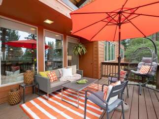 Enjoy outdoor living on this spacious deck featuring a comfortable seating area with a gray sofa, accent chairs, and a coffee table, all complemented by a vibrant orange and white striped rug.