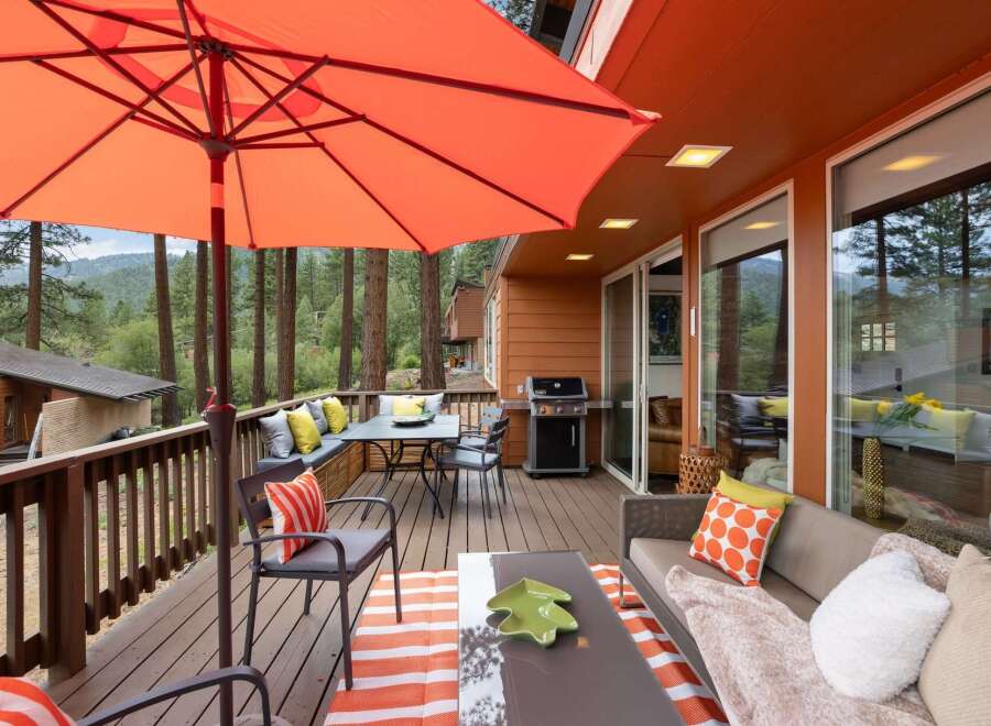 Enjoy outdoor living at its finest on this spacious deck, complete with a dining area under a large orange umbrella and a comfortable seating area with a sofa and accent pillows.
