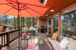 Enjoy outdoor living at its finest on this spacious deck, complete with a dining area under a large orange umbrella and a comfortable seating area with a sofa and accent pillows.