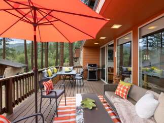 Enjoy outdoor living at its finest on this spacious deck, complete with a dining area under a large orange umbrella and a comfortable seating area with a sofa and accent pillows.