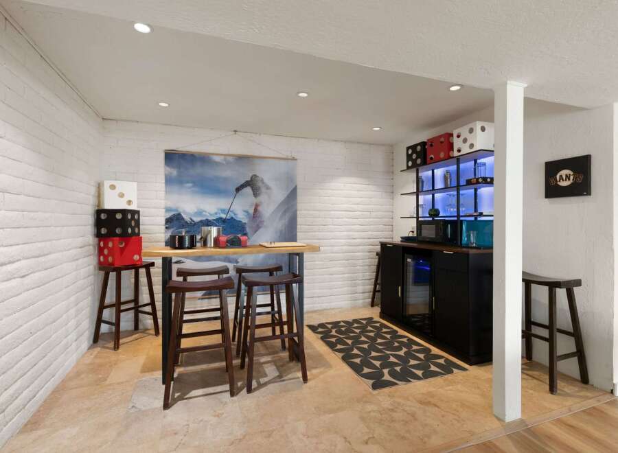This basement bar area features a unique ski-themed mural and a modern bar with a built-in cooler.