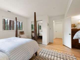 Experience serene living in this charming bedroom, featuring large windows that frame picturesque forest views.