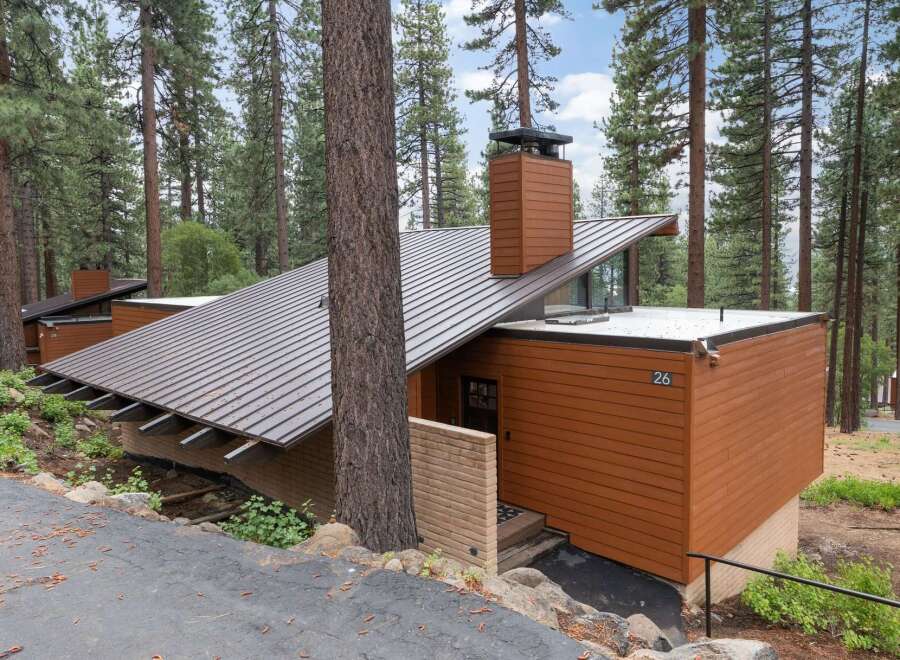 Nestled among tall pine trees, this modern mountain home features a striking asymmetrical metal roof and warm wood siding.