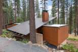 Nestled among tall pine trees, this modern mountain home features a striking asymmetrical metal roof and warm wood siding.