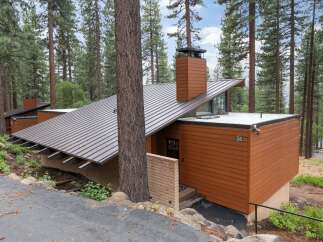 Nestled among tall pine trees, this modern mountain home features a striking asymmetrical metal roof and warm wood siding.