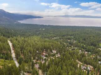 Nestled amidst a dense forest of towering pine trees, this property offers a serene escape with stunning views of a vast, tranquil lake and distant mountains.