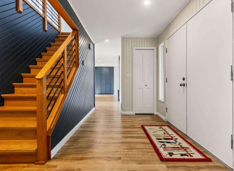 Step into this inviting entryway featuring a striking dark wood paneled accent wall alongside a beautiful natural wood staircase.