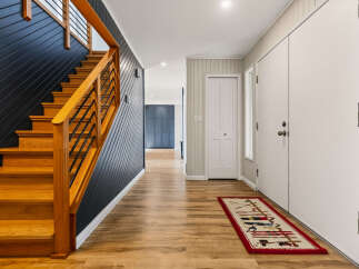 Step into this inviting entryway featuring a striking dark wood paneled accent wall alongside a beautiful natural wood staircase.