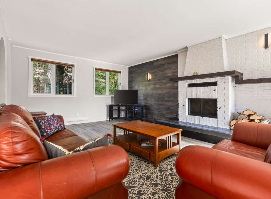 Cozy up by the brick fireplace in this inviting living room, featuring warm leather sofas and a rustic wood accent wall.
