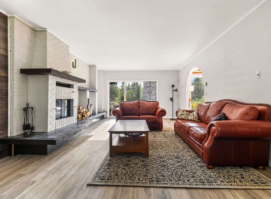 This spacious living room features a striking white brick fireplace with a dark wood mantel, complemented by a rustic wood-paneled accent wall.