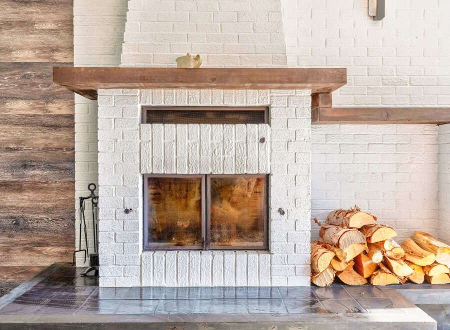 Cozy up by this stunning white brick fireplace, featuring a rustic wooden mantel and double glass doors for a clear view of the fire.