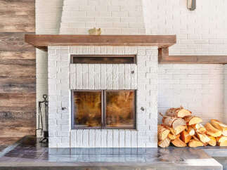 Cozy up by this stunning white brick fireplace, featuring a rustic wooden mantel and double glass doors for a clear view of the fire.