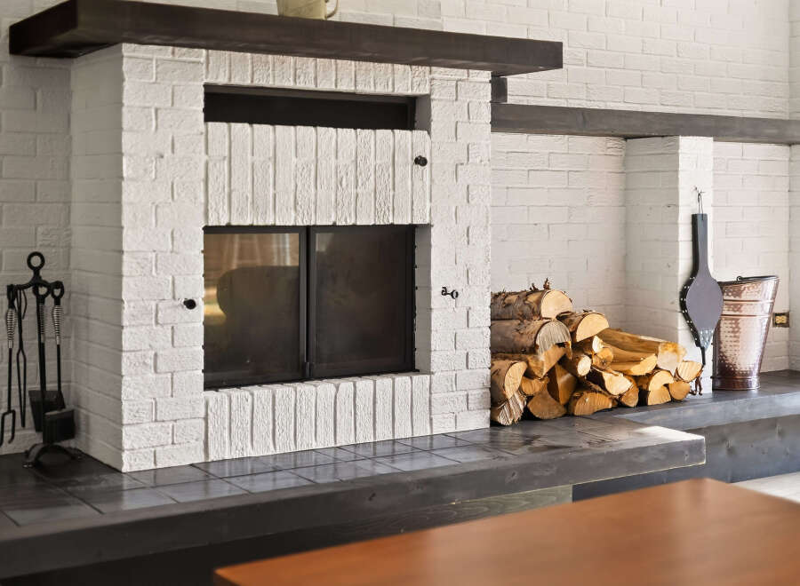 Cozy up by the fireplace in this charming living space, featuring a classic white brick hearth and a rustic wood mantel.