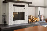 Cozy up by the fireplace in this charming living space, featuring a classic white brick hearth and a rustic wood mantel.