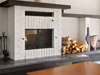 Cozy up by the fireplace in this charming living space, featuring a classic white brick hearth and a rustic wood mantel.