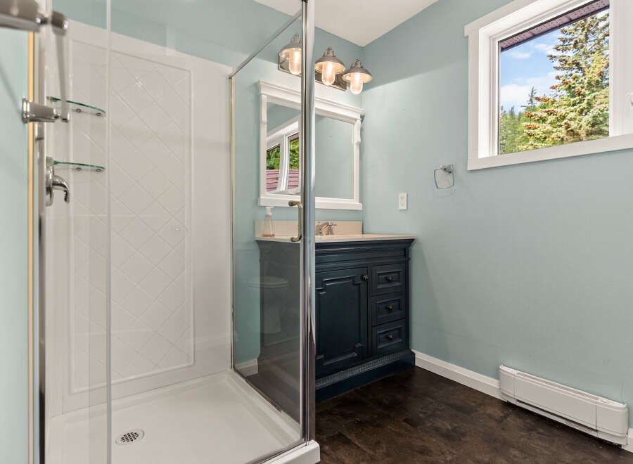 This charming bathroom features a spacious glass-enclosed shower with convenient shelving.
