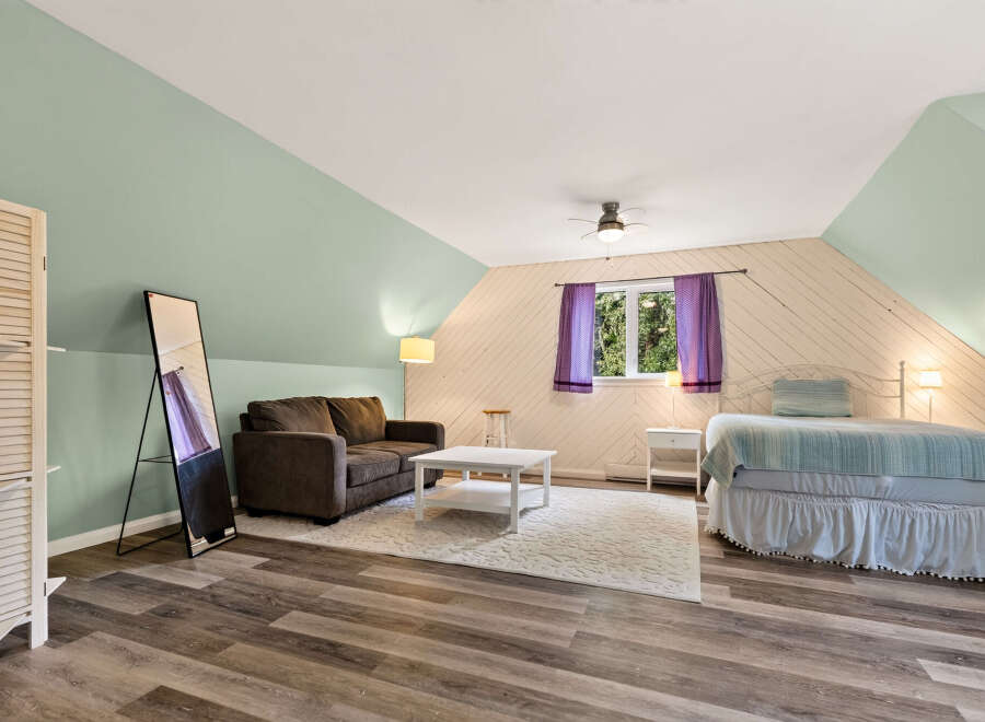 This charming attic bedroom features a cozy seating area with a dark brown sofa and a white coffee table, perfect for relaxation.