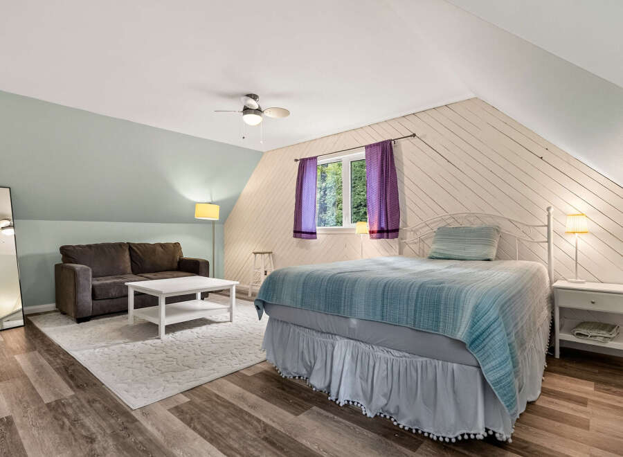 Discover this charming attic bedroom featuring a cozy seating area with a plush sofa and a modern coffee table, perfect for relaxation.